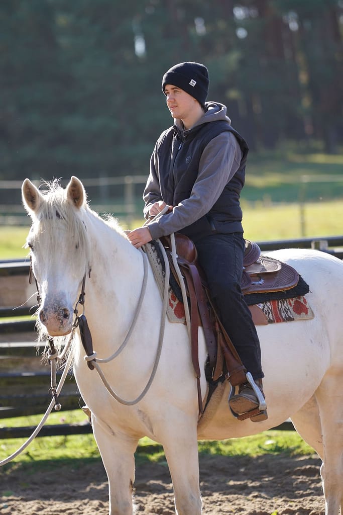 Western-Reiter im Outdoor-Training auf hellem Pferd, Ranch-Gelände mit Wald und Weide im Hintergrund